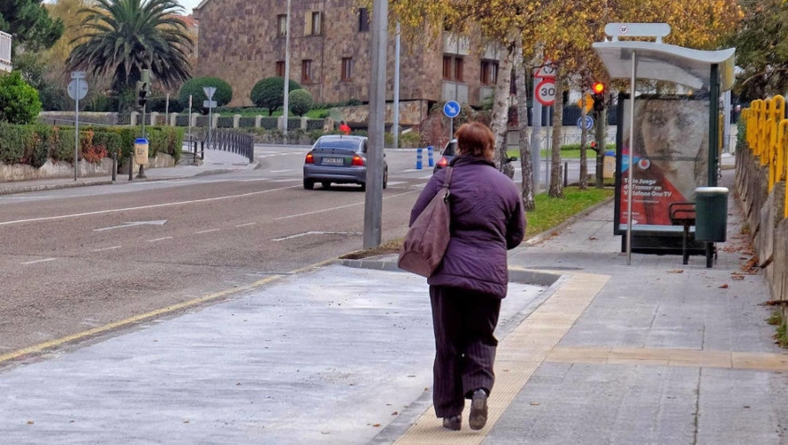 Mujer caminando hacia una marqueisna de autobús por una calle de Santander.